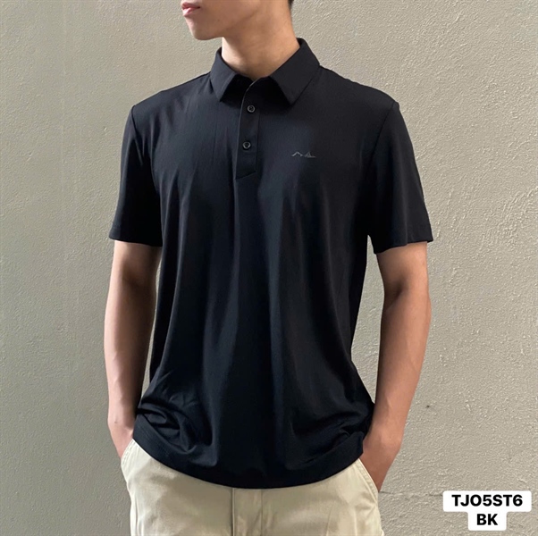 Áo polo nam ngắn tay màu đen, cổ bẻ ba khuy, logo nhỏ ở ngực, người mẫu mặc đứng thẳng trước tường be