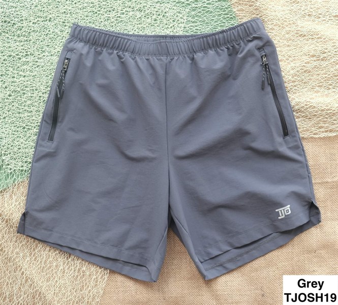 Quần short xám trải phẳng trên nền lưới và bao tải, cạp chun, túi khoá kéo hai bên, logo nhỏ ở ống