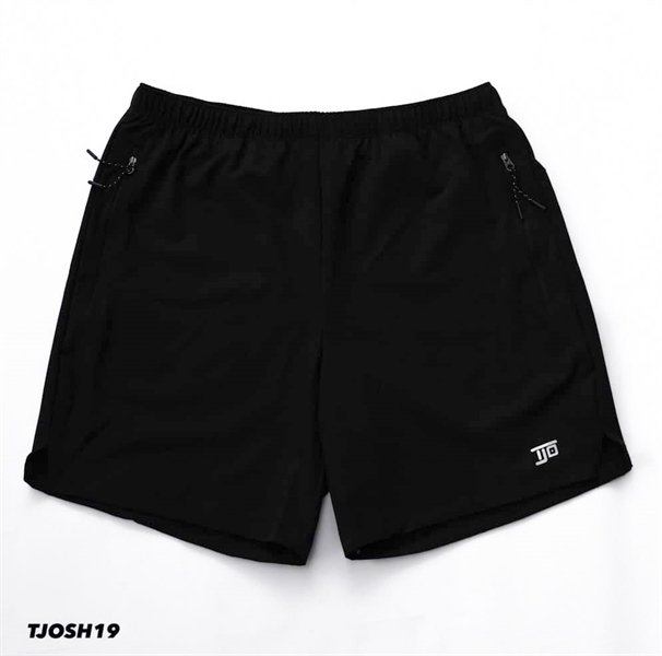 Quần short đen trải phẳng mặt trước, cạp chun, hai túi khoá kéo, gấu xẻ hai bên, logo nhỏ ở ống